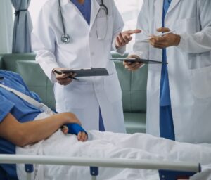 Injured patient with a bandaged wrist and arm shows doctor in a hospital office. Nurse assists with first aid for a sprain or fracture.