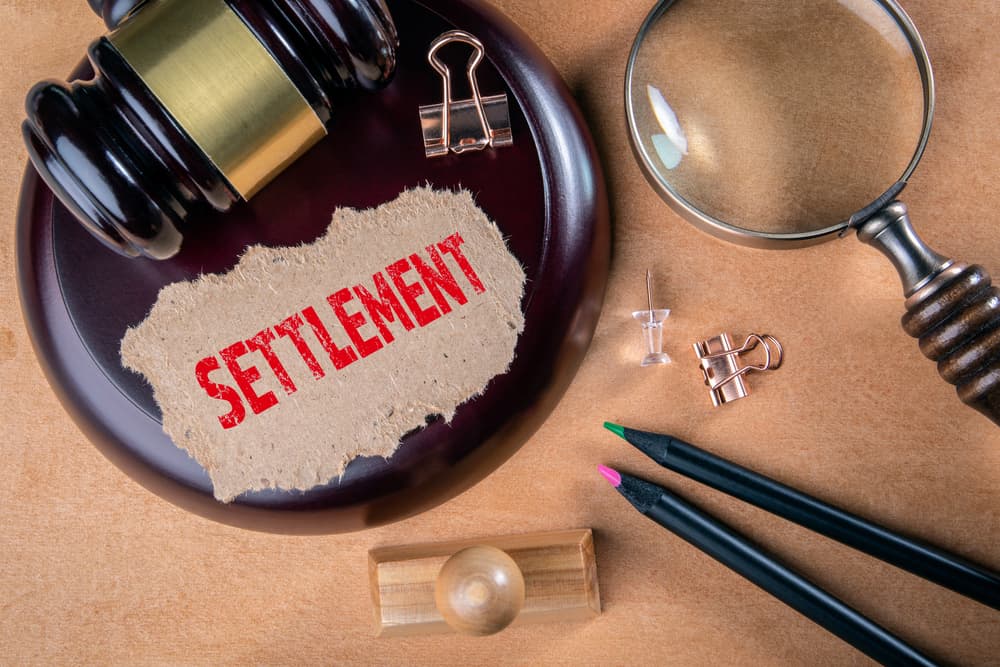 Gavel with 'Settlement' paper, magnifying glass, and office supplies on a desk.