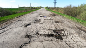 Cracked, weathered asphalt on Forest Hill Blvd and Military Trail, riddled with potholes, creating a hazardous driving environment.