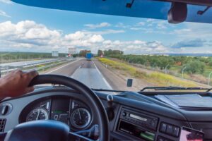 View of a rear-end collision from the driving position of a truck, showing a vehicle in front and a landscape with clouds.