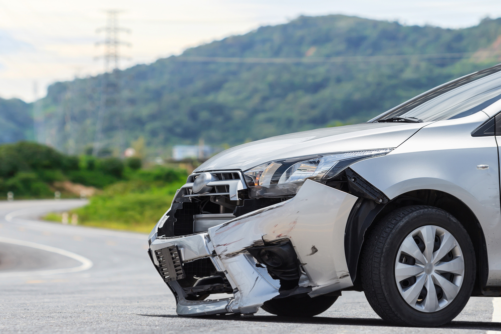 The front of a silver car is damaged from a crash on the road, highlighting the need for car repair or insurance.