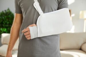 A person wearing a grey shirt has their arm in a medical sling, indicating an injury from an accident.