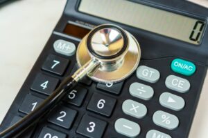 A stethoscope and calculator on a table symbolize the financial burden of medical expenses.