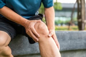 A person sitting down, holding their knee with both hands, appearing to be in pain.