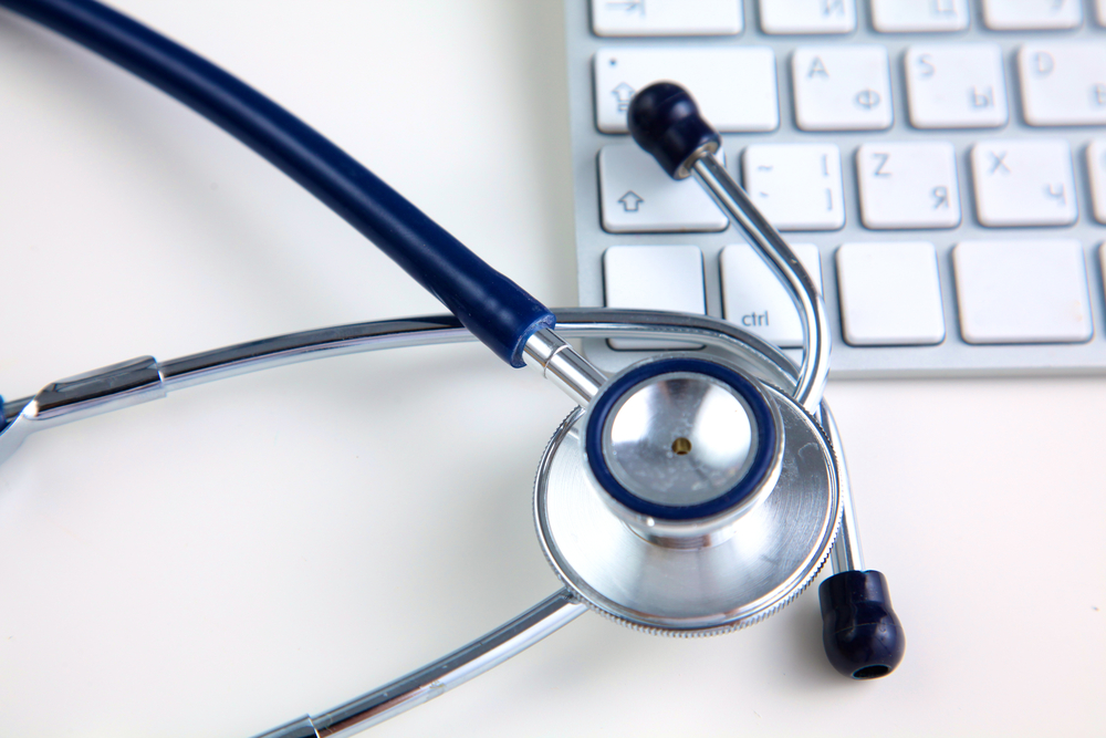 A medical stethoscope near a laptop on a wooden table, on white