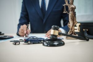 Legal professional at desk with gavel, scales, and car model, symbolizing car accident legal assistance.