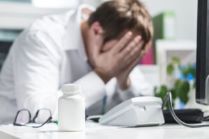 Stressed doctor with head in hands, feeling pressured while addressing claims of patient negligence.