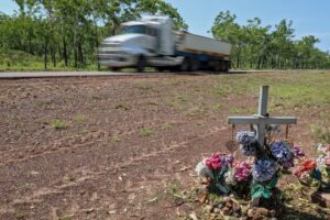 Cross next to road. Commemorate death of loved one, family, friend. Speeding truck passing by. Road safety, death toll, statistics, fatal accident or crash, traffic